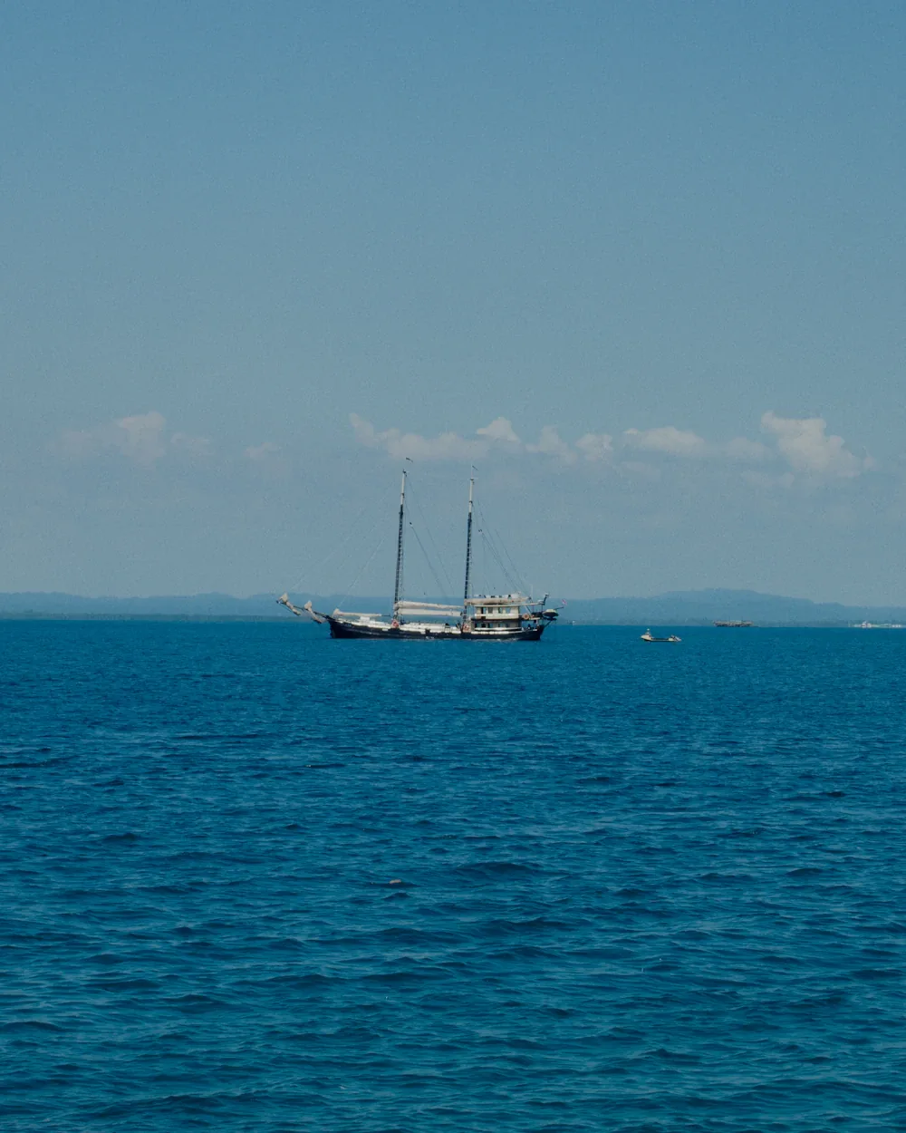 Two-masted phinisi schooner on open blue water, headed east