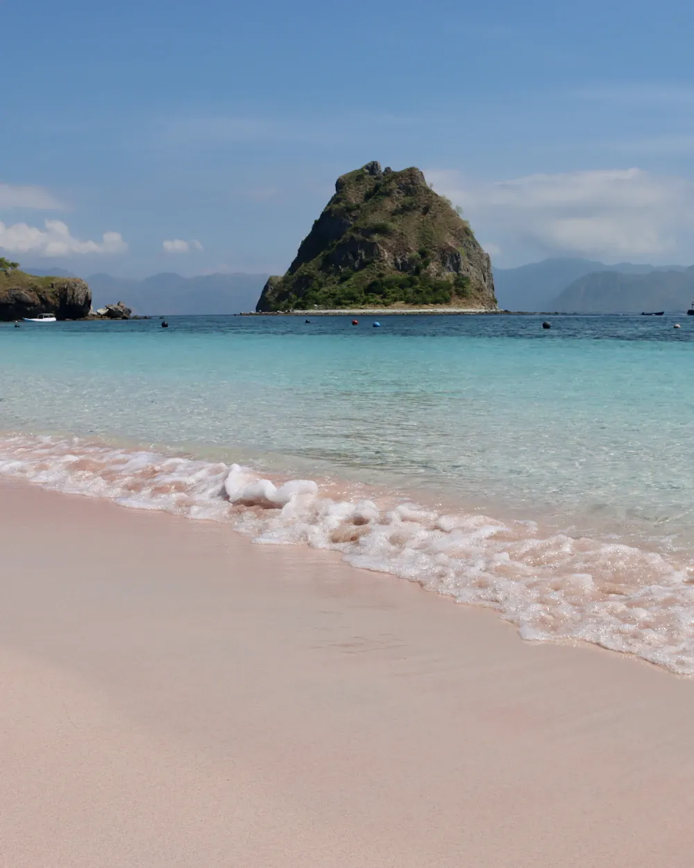 Pink-tinged sand and clear water with a rock offshore