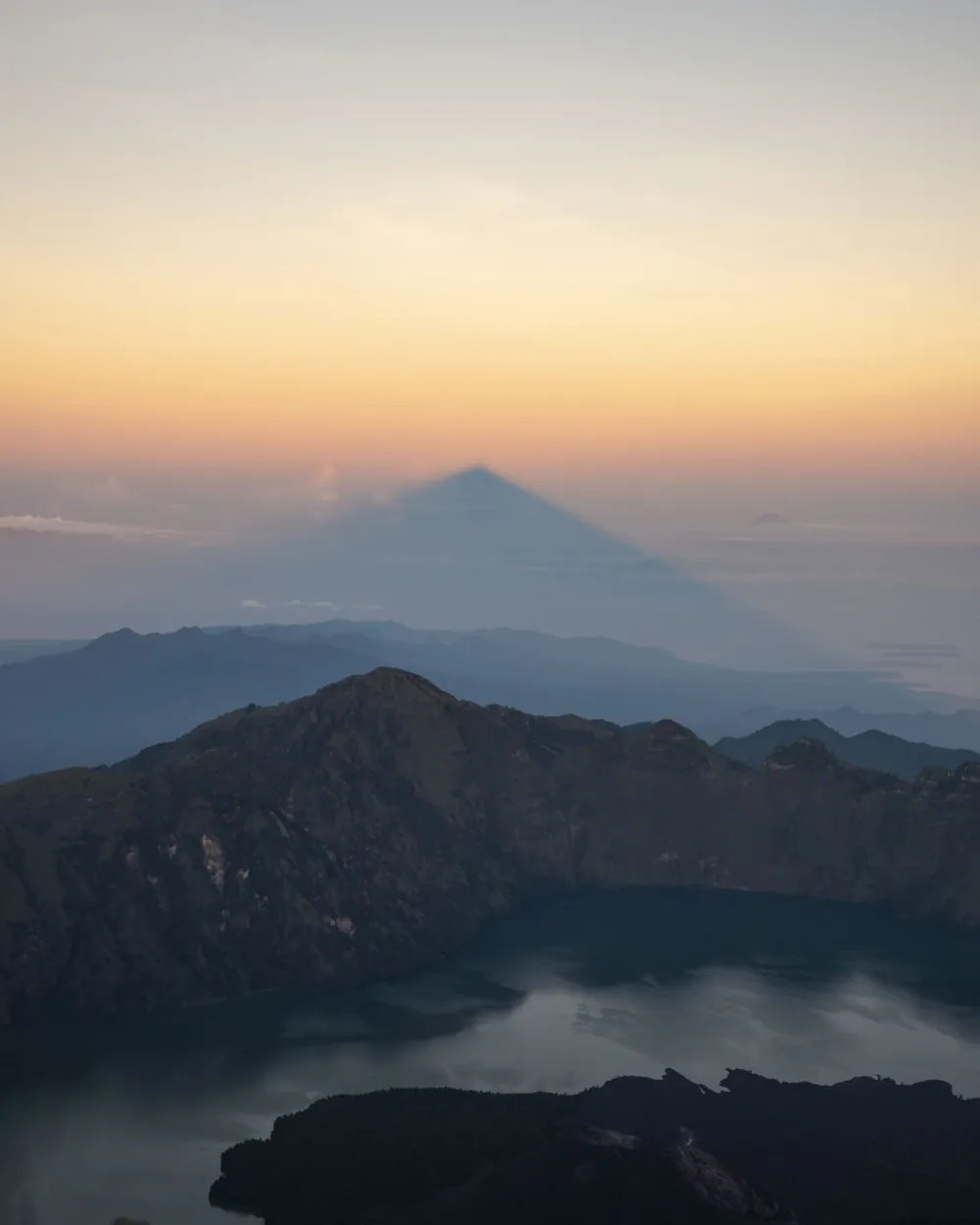 Mount Rinjani casting its summit shadow at sunrise, above the caldera and Segara Anak crater lake