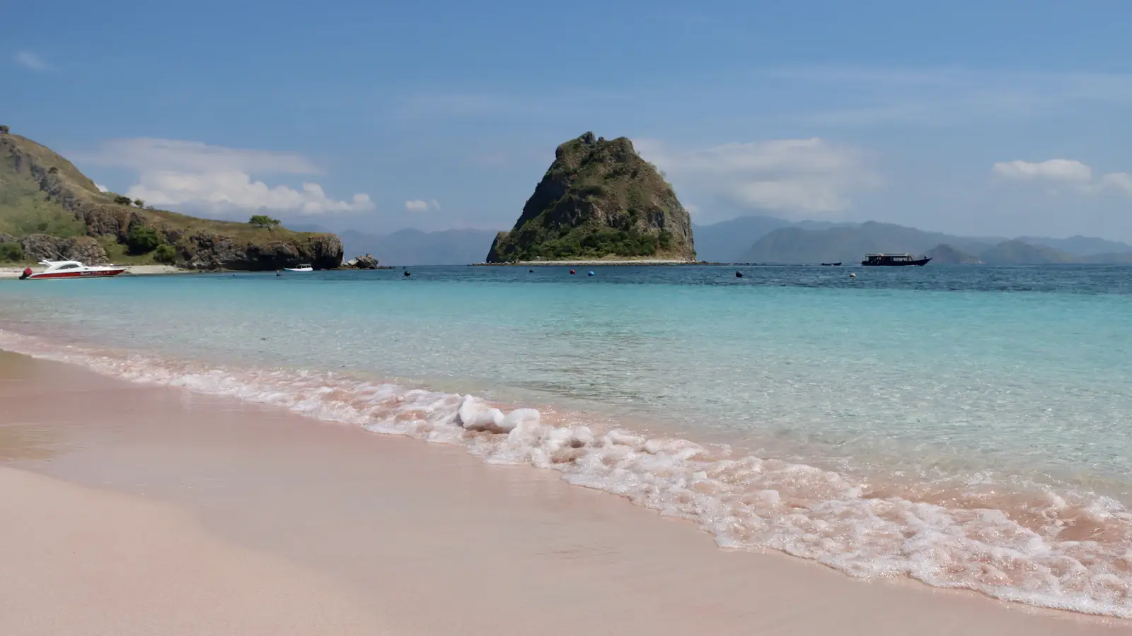 Pink-tinged sand and clear water with a rock offshore