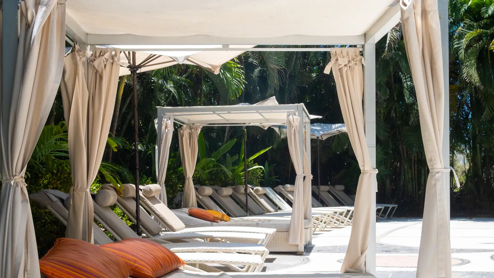 Shaded daybeds and cabanas beside a quiet pool